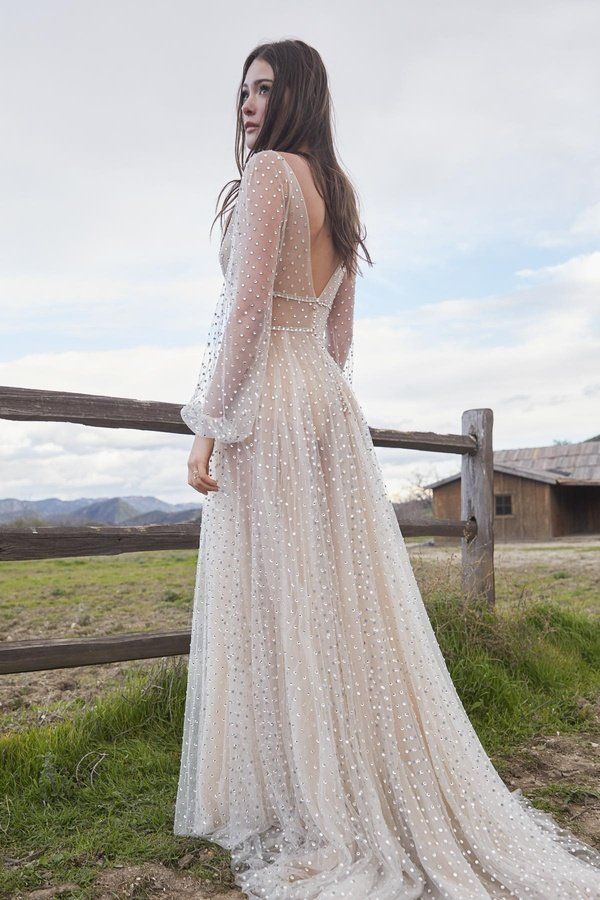 Eine Frau in einem Brautkleid steht neben einem Holzzaun auf einem Feld.