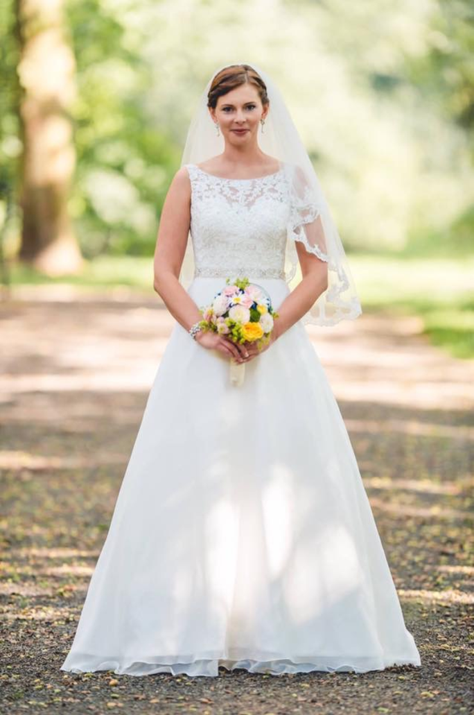 Die Braut trägt ein weißes Brautkleid und hält einen Blumenstrauß in der Hand.