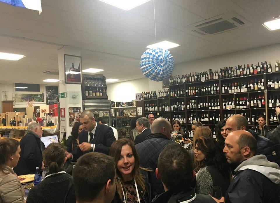 Un gruppo di persone socializza in un'enoteca, con file di bottiglie sugli scaffali sullo sfondo.
