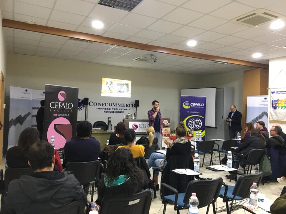 Un oratore si rivolge a un pubblico in una sala conferenze arredata con striscioni aziendali, file di sedie e attrezzature per presentazioni.