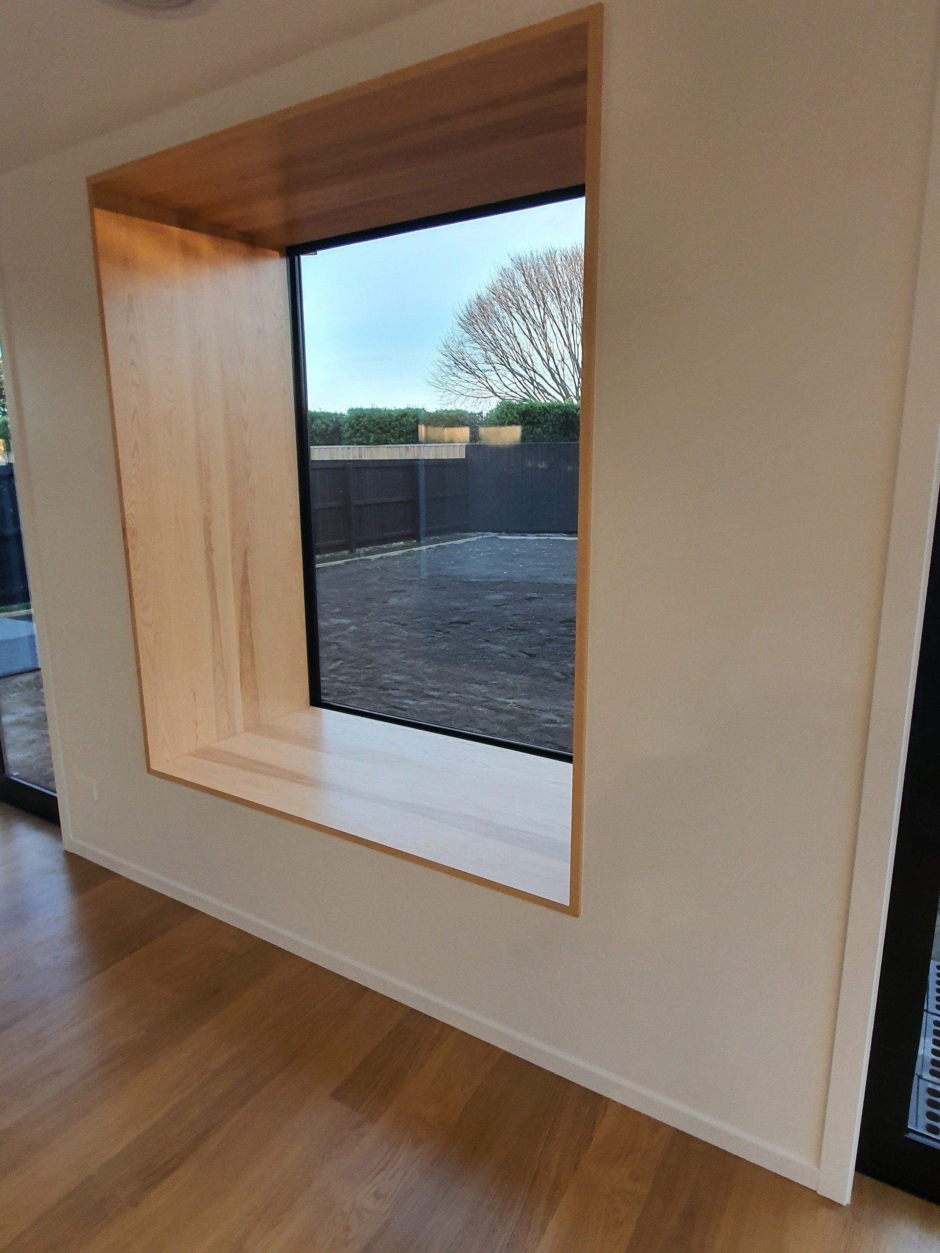 A large window with a wooden frame in a room with hardwood floors.