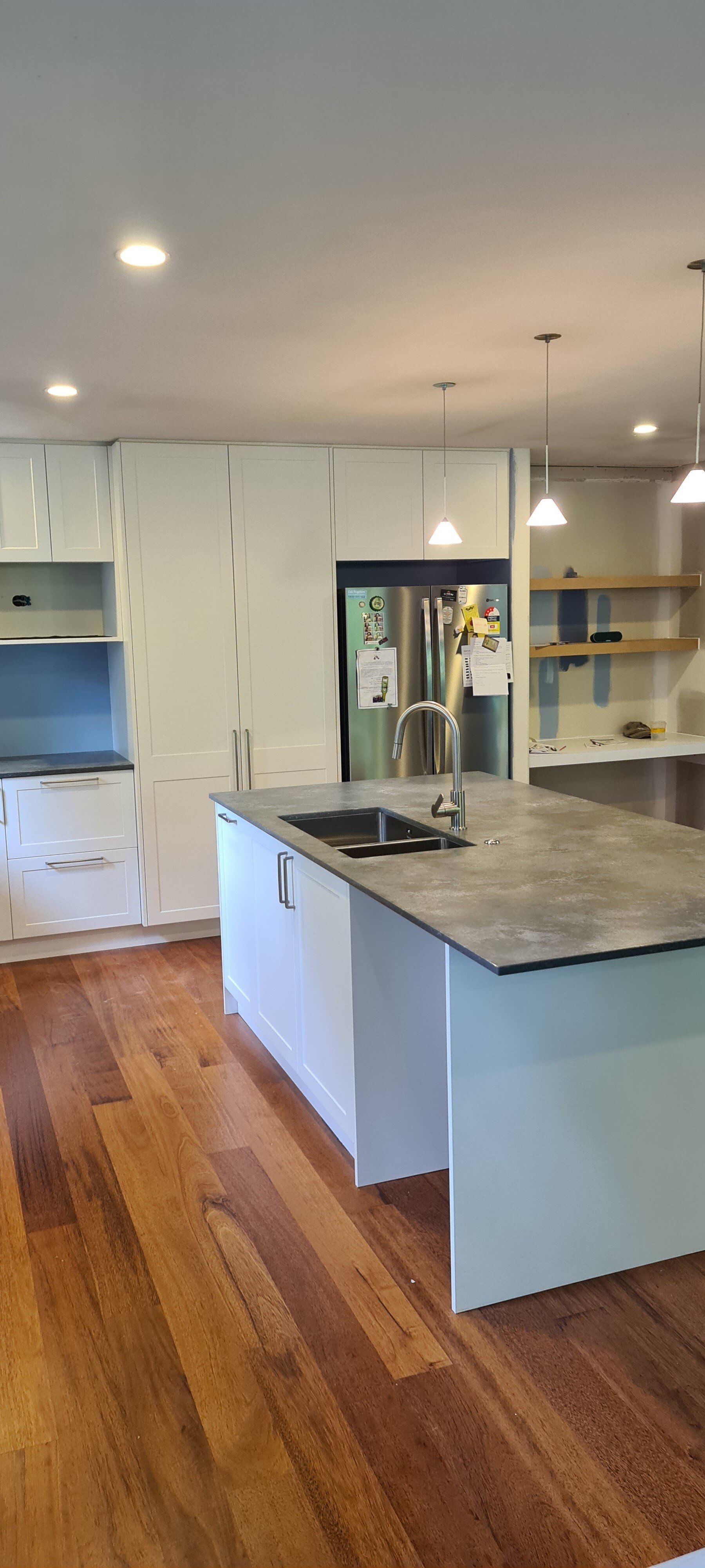 A kitchen with a large island , sink , refrigerator and wooden floors.