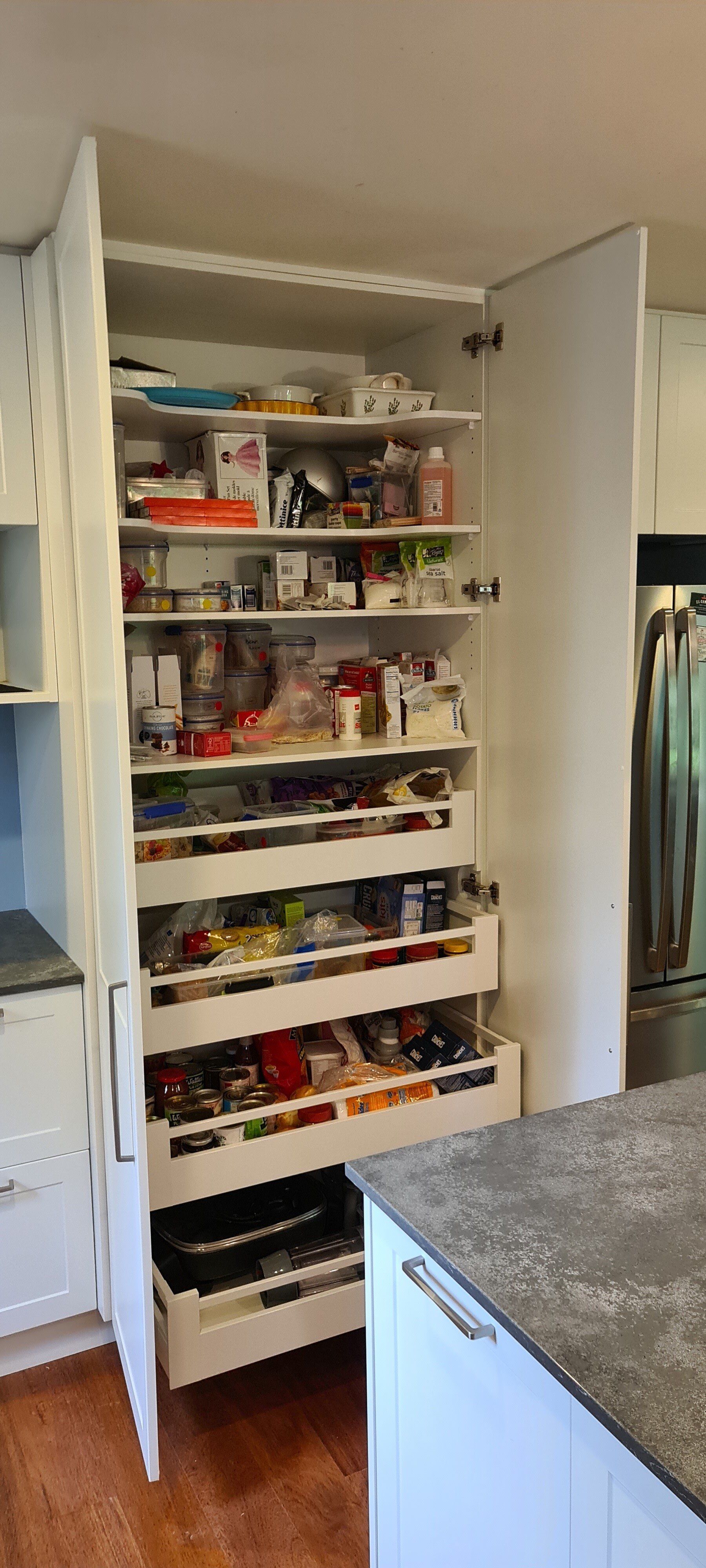 A kitchen pantry with drawers and shelves filled with food.