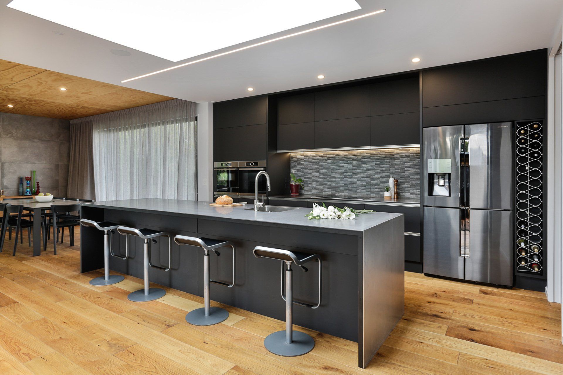 A kitchen with a large island , stools , a refrigerator and a wine rack.