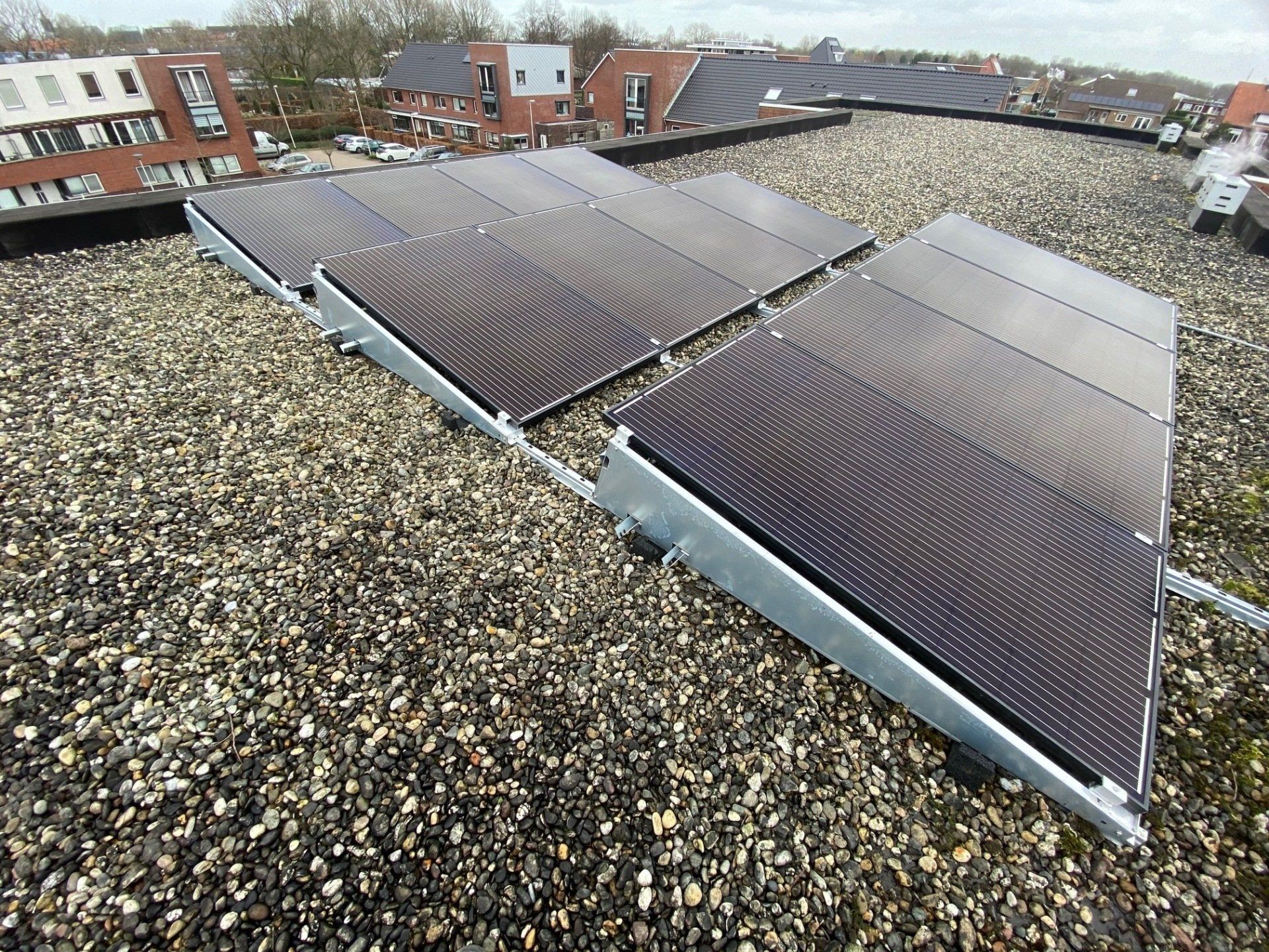 Zonnepanelen geïnstalleerd op een plat grinddak, met een woongebouw zichtbaar op de achtergrond.
