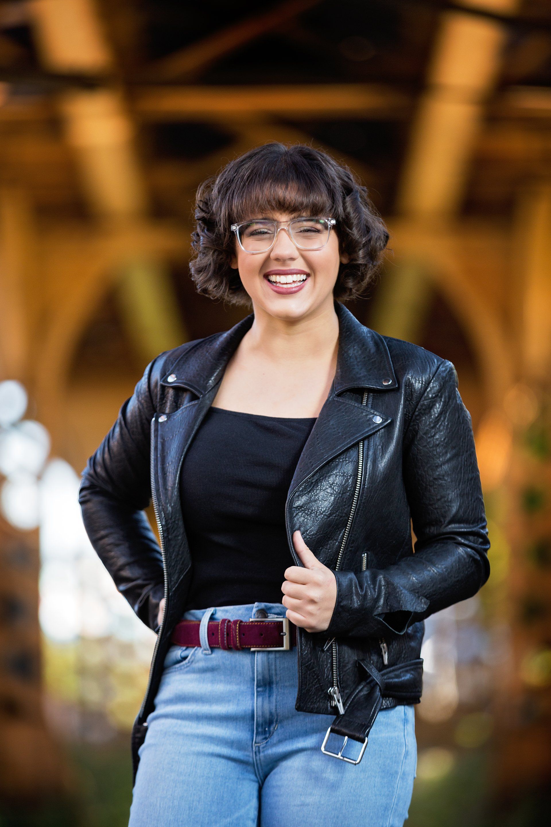 A woman wearing glasses and a leather jacket is smiling for the camera.