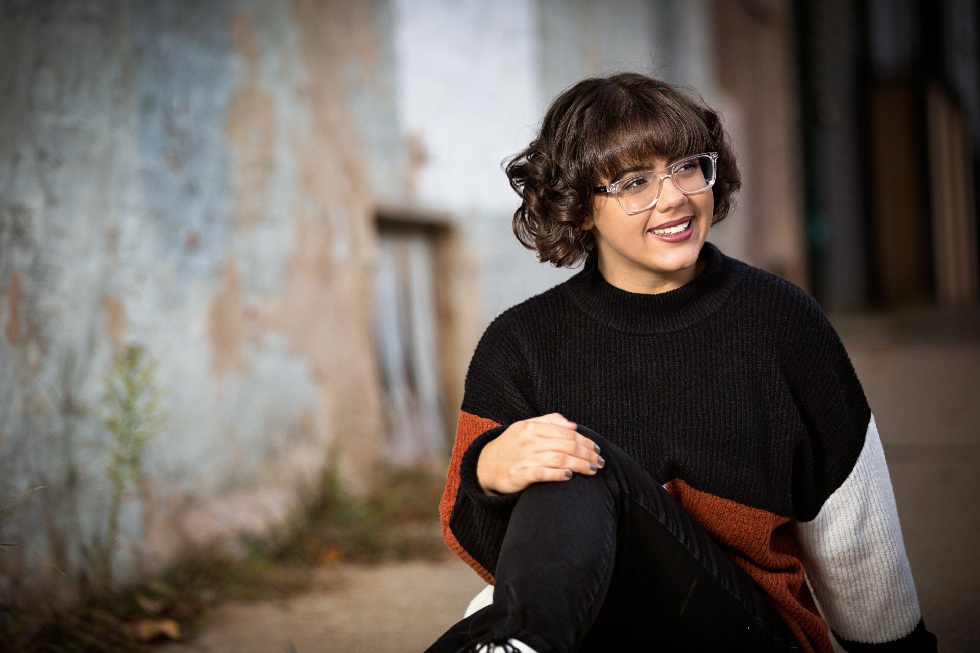 A woman wearing glasses and a black sweater is sitting on the ground.