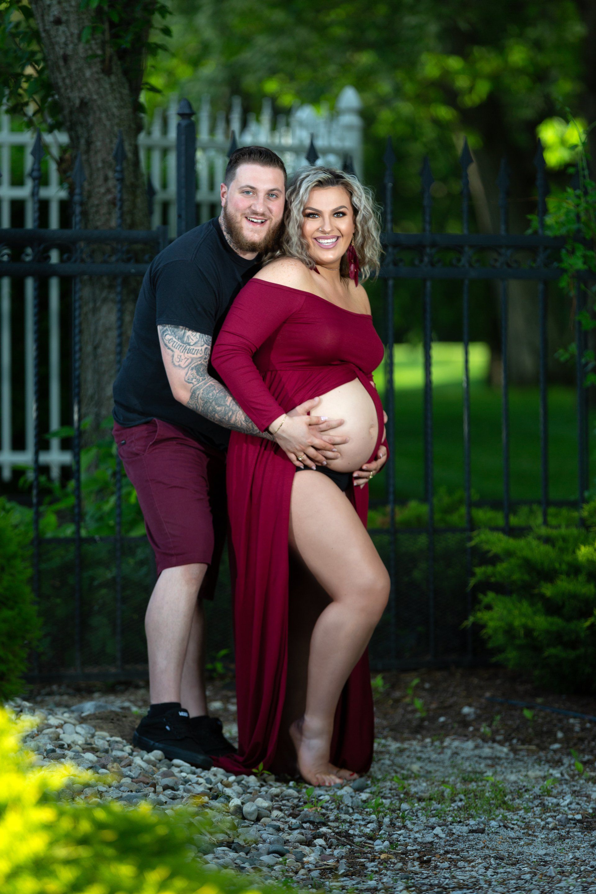 A man is hugging a pregnant woman in a red dress.