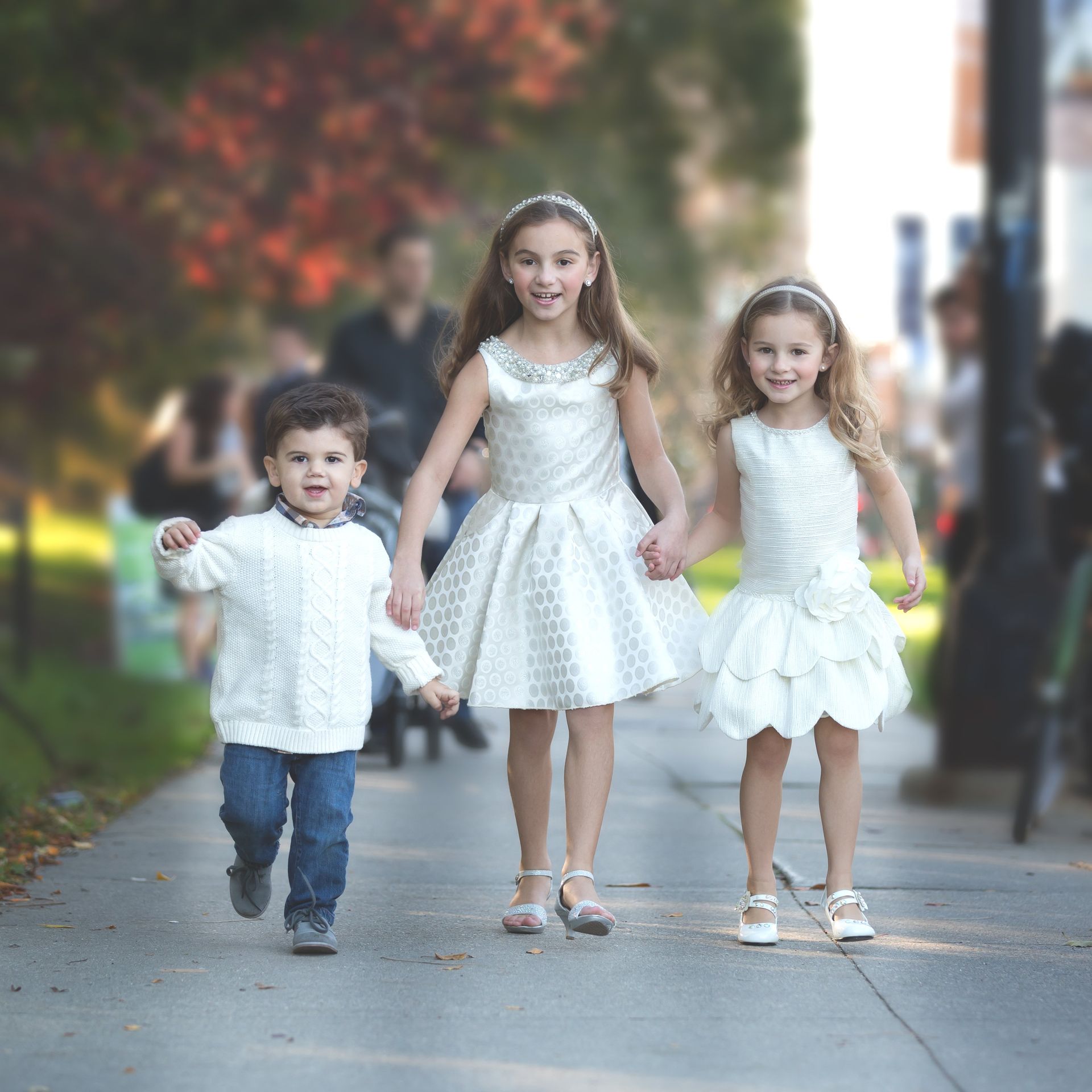 A boy and two girls are walking down a sidewalk holding hands