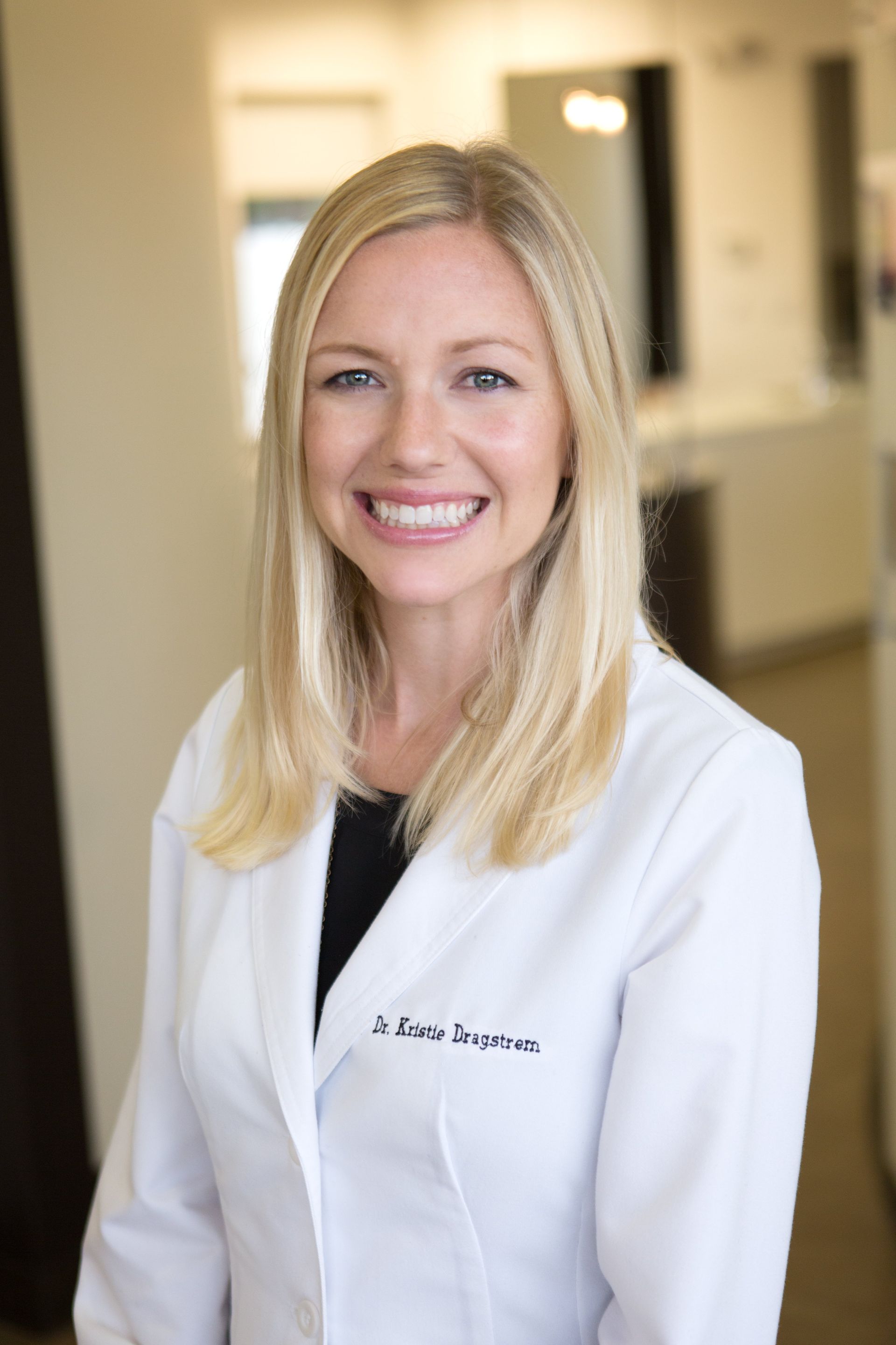 A woman in a white lab coat is smiling for the camera.