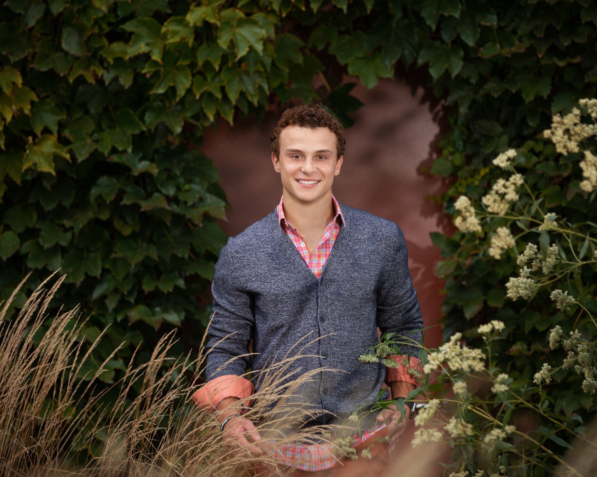 A young man in a blue sweater is standing in front of a wall.