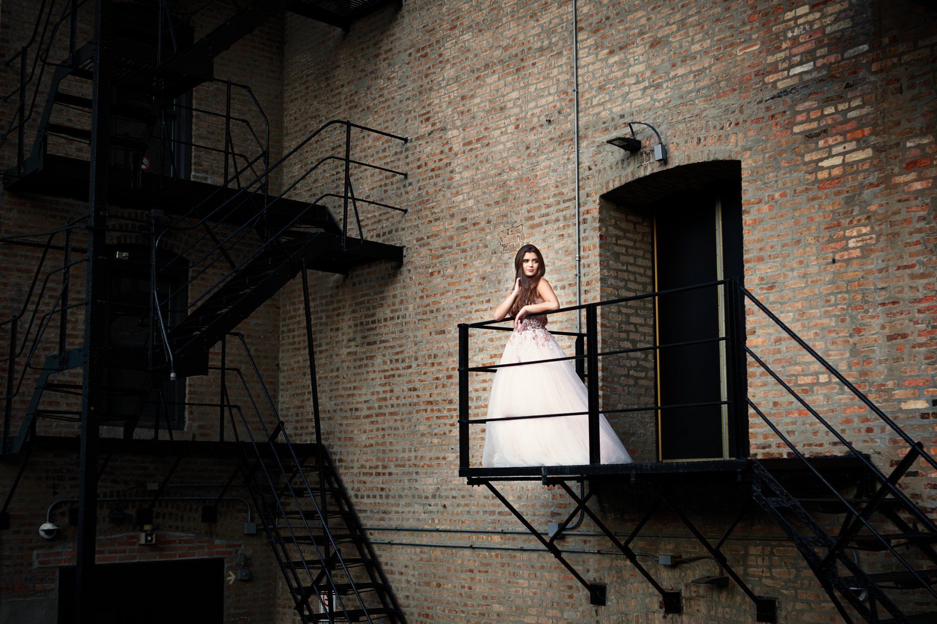 A bride in a wedding dress is standing on a fire escape.