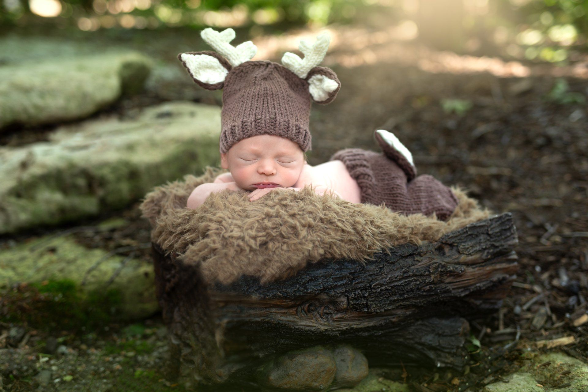A newborn baby is wearing a reindeer hat and laying in a log.