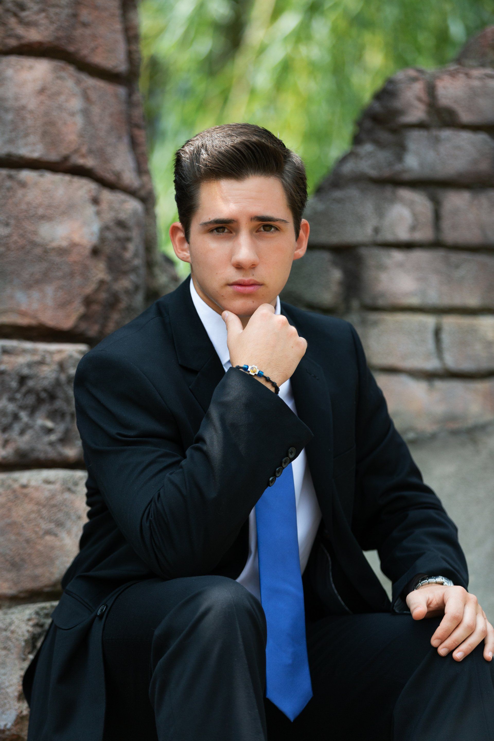 A man in a suit and tie is sitting in front of a stone wall.