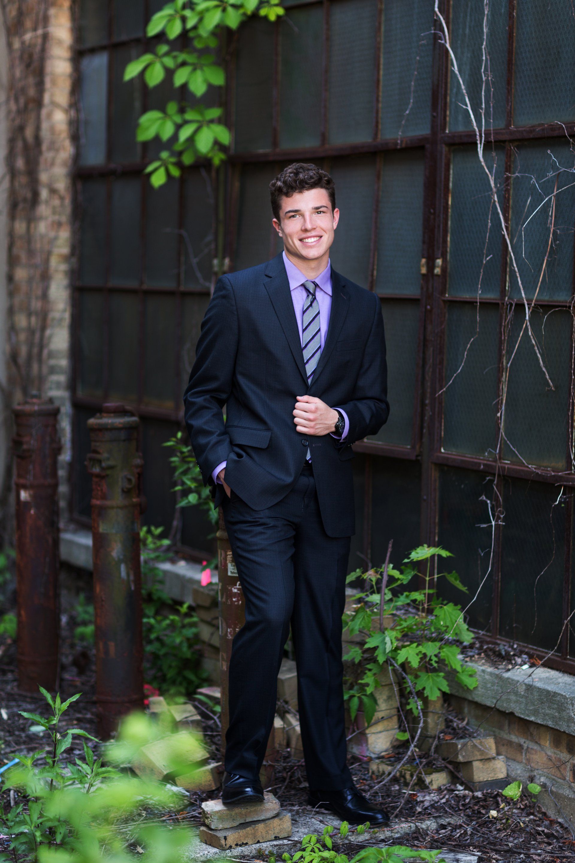 A young man in a suit and tie is standing in front of a building.