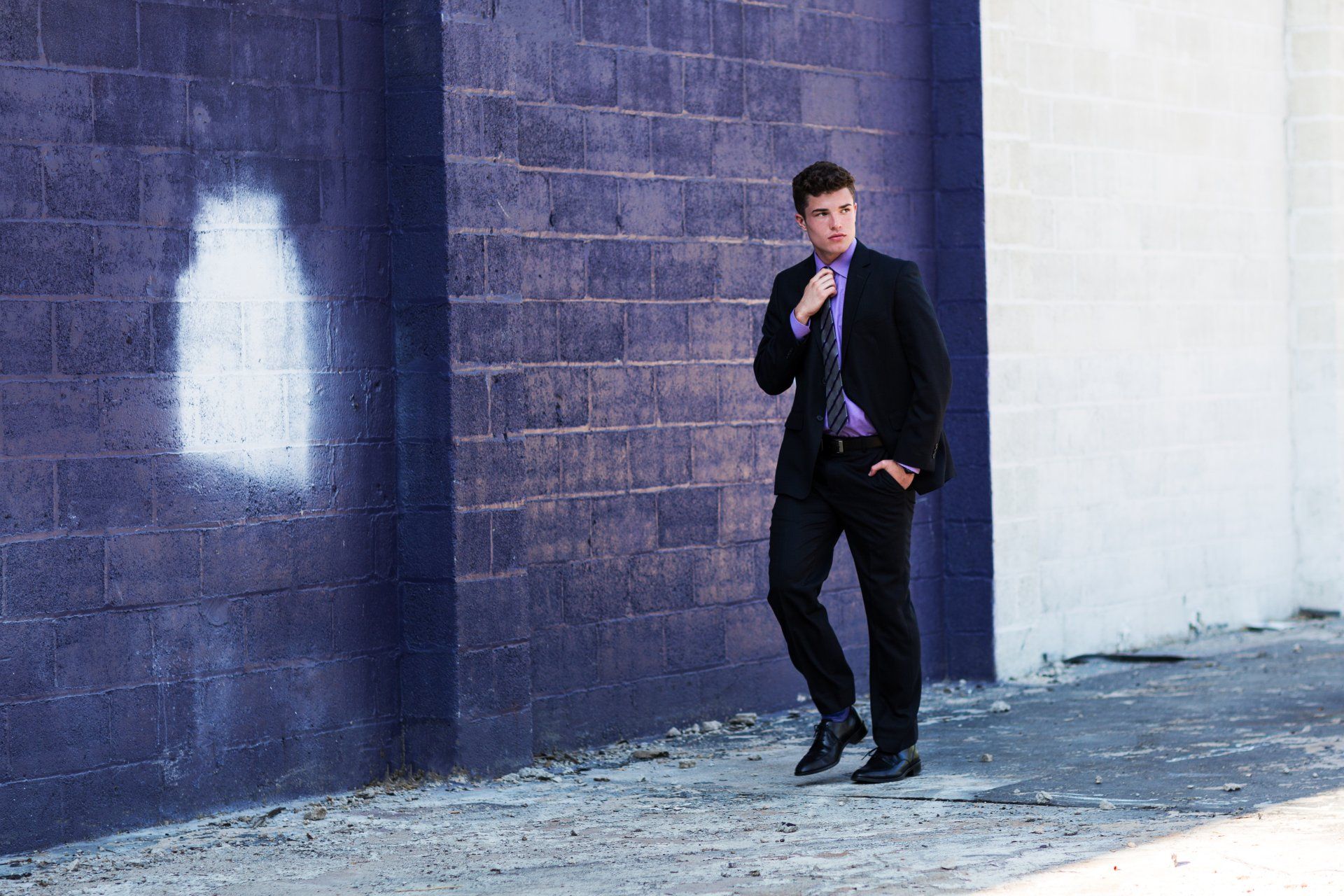 A man in a suit and tie is standing in front of a purple brick wall.