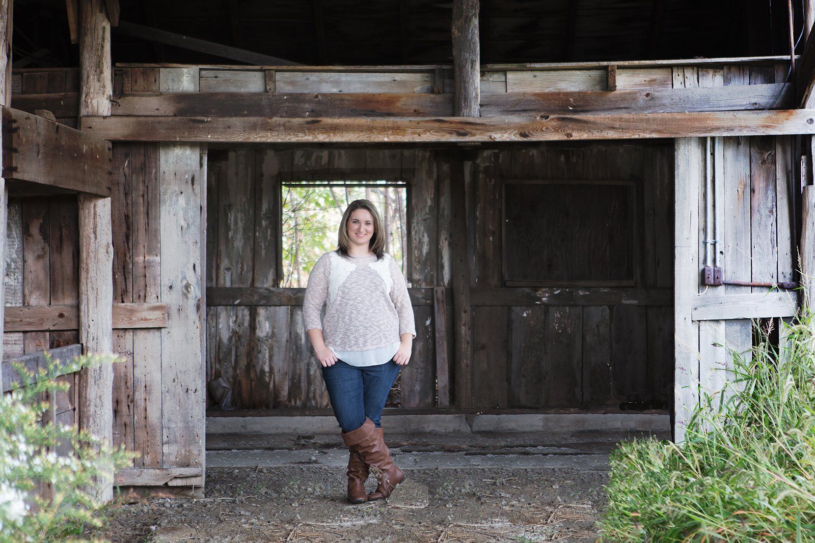 A woman is standing in front of an old wooden barn.