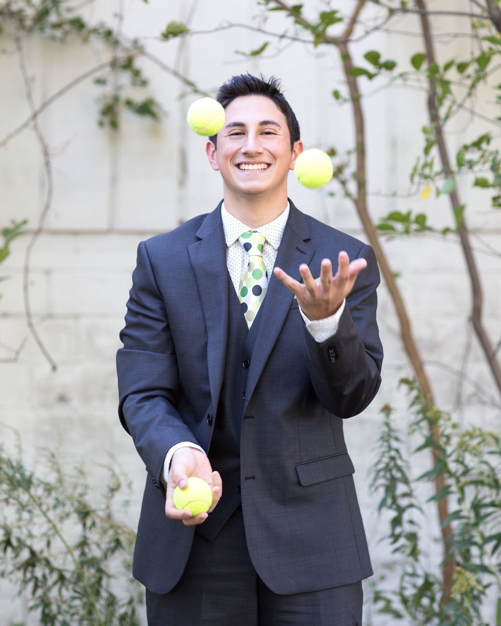 A man in a suit and tie is juggling tennis balls