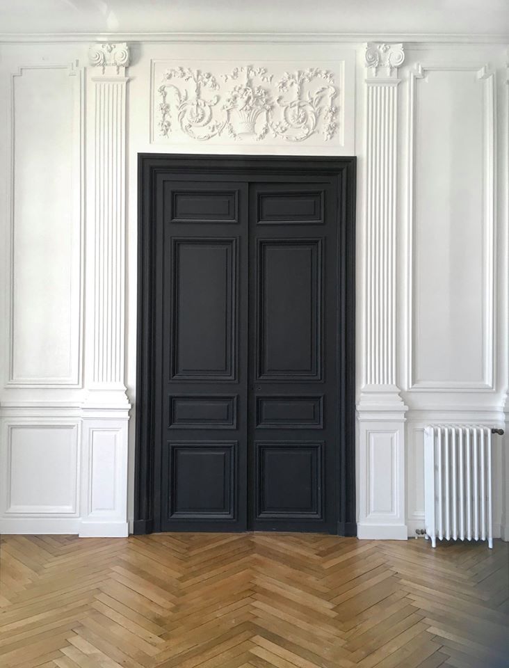 Une pièce avec une porte noire et un plancher en bois.