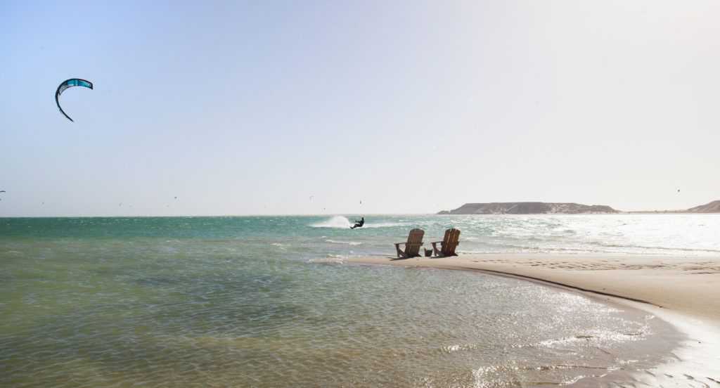 Deux chaises sont assises sur une plage de sable à côté de l'océan.