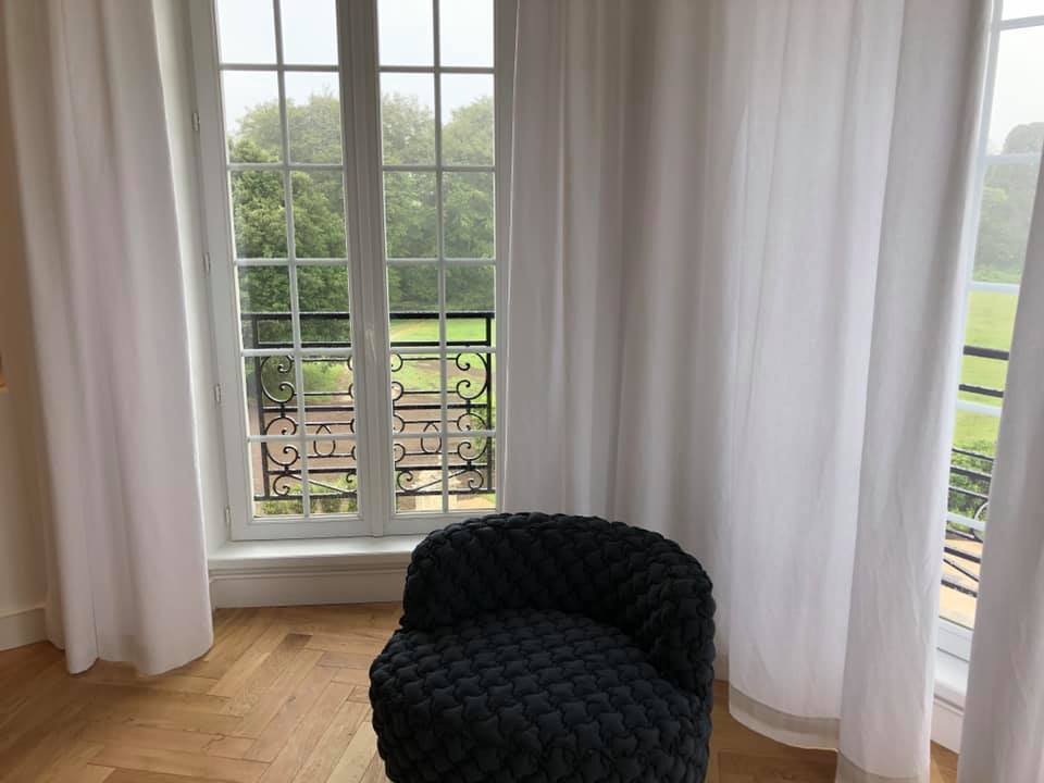 Une chaise est assise devant une fenêtre avec des rideaux blancs.