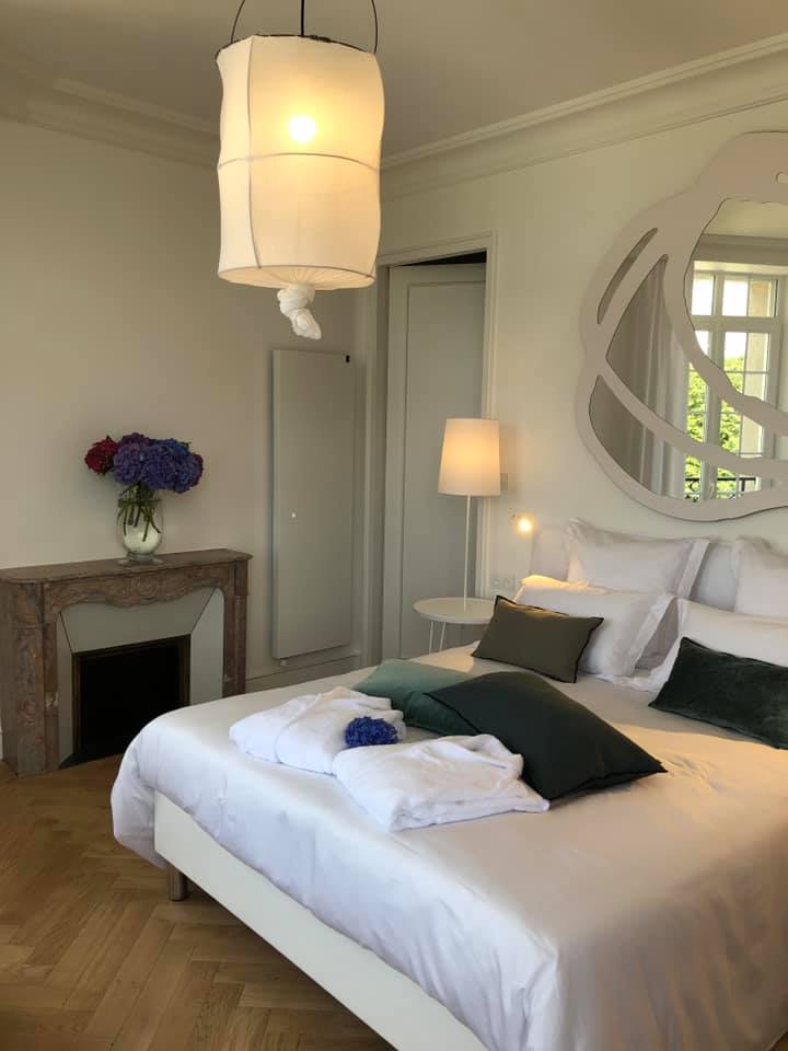 Une chambre avec un grand lit, cheminée, lampe et miroir.