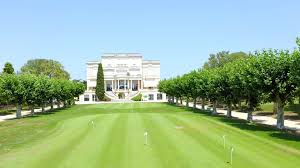 Il y a un grand bâtiment en arrière-plan et un terrain de golf au premier plan.