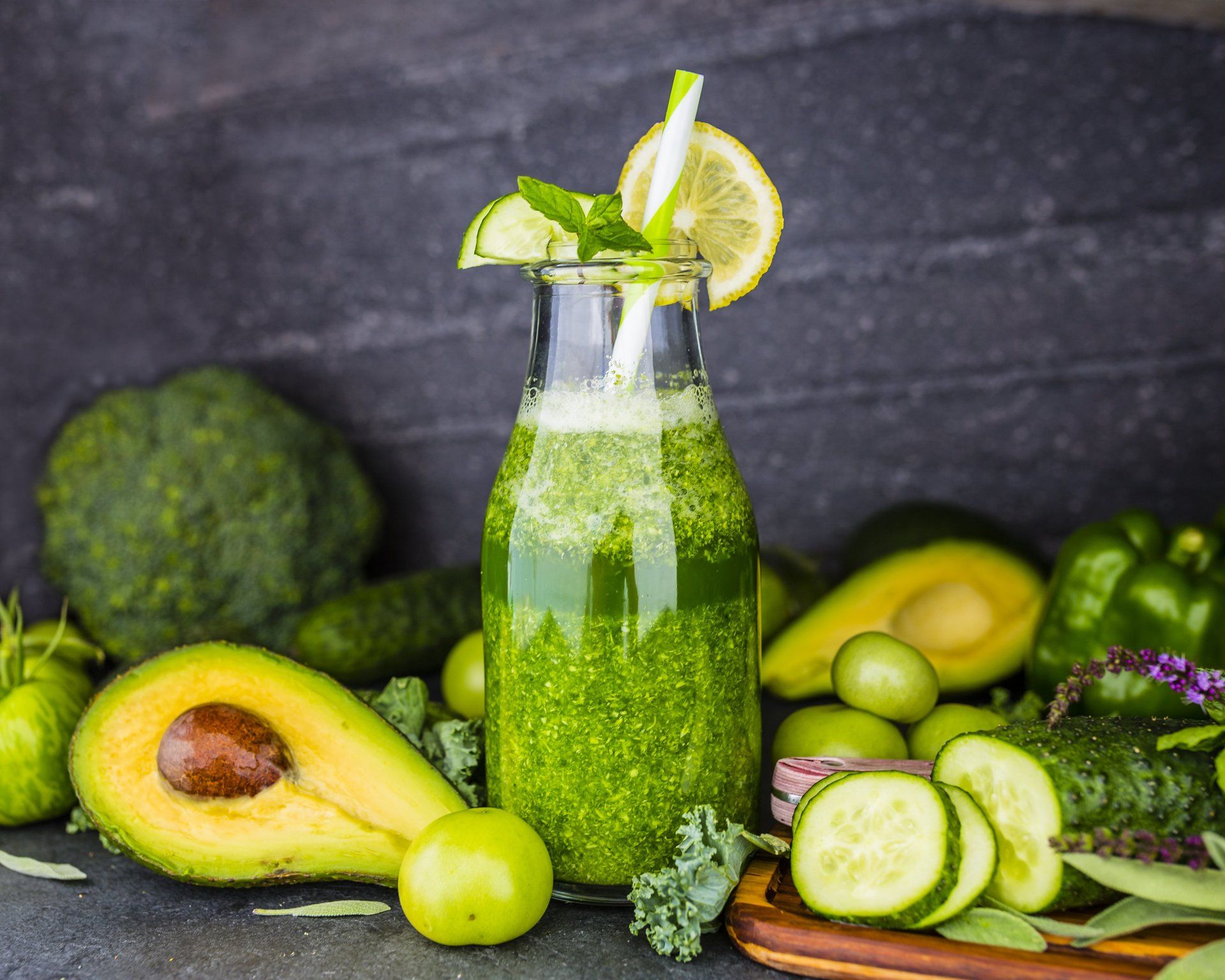 Un smoothie vert dans une bouteille avec une paille entourée de légumes.