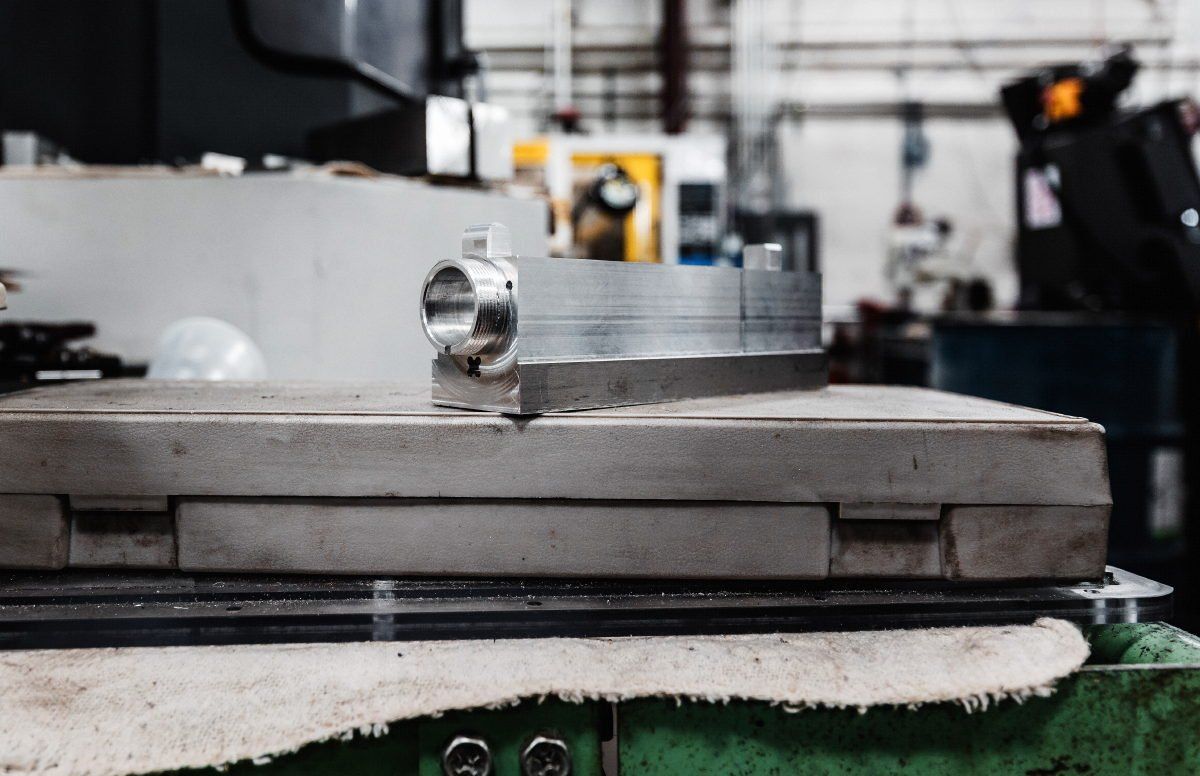 A metal workpiece on a machine table in a workshop, close-up with the machine's background blurred.