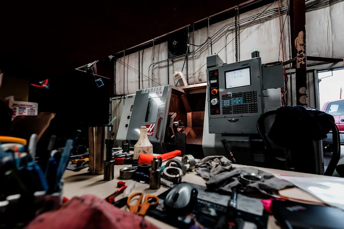 Workshop interior with tools, machinery, and a cluttered workbench. Gray CNC machine, metal walls.
