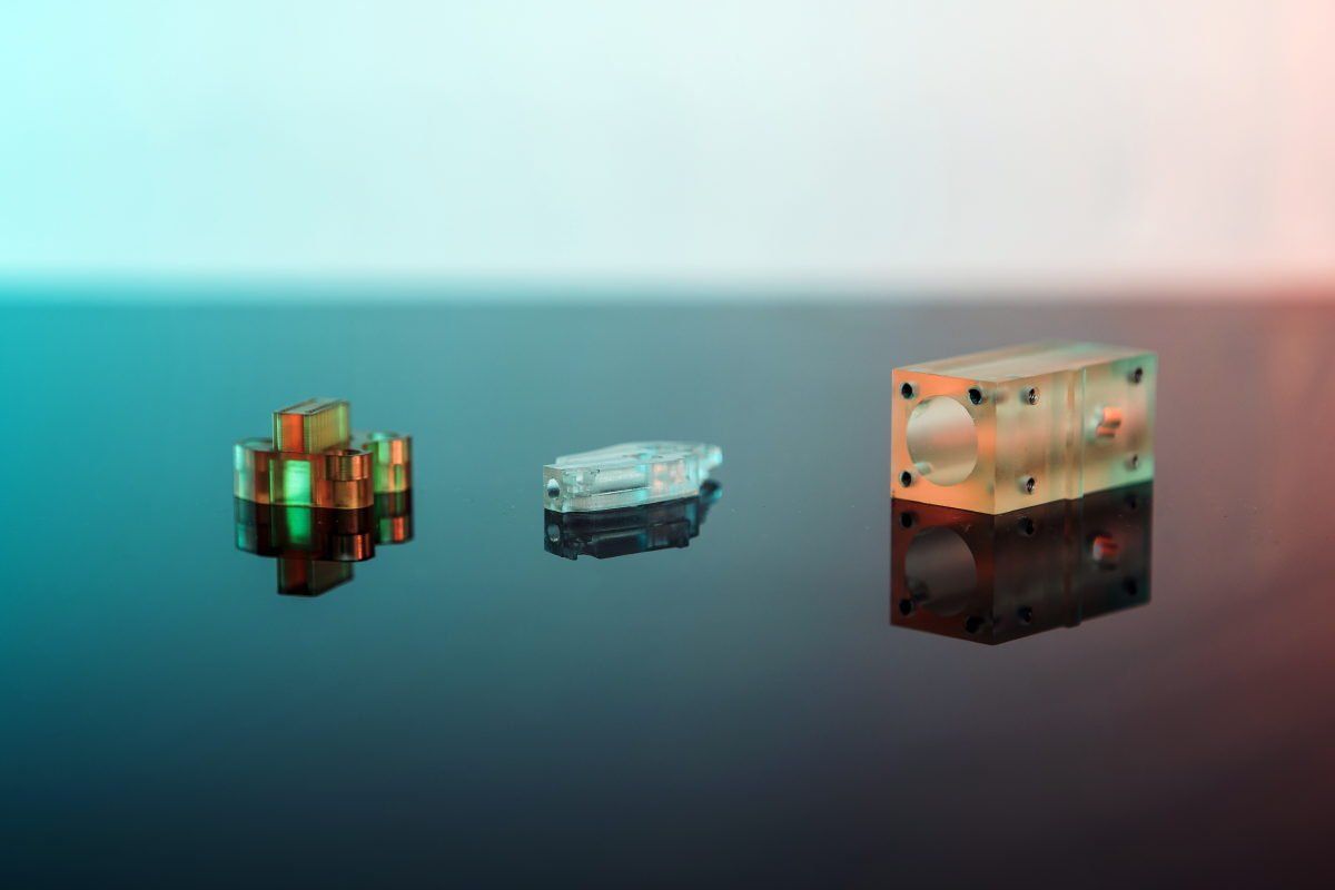 Three glowing geometric objects on a reflective surface: a gold-green cube, a gray-white crystal, and a brown block.