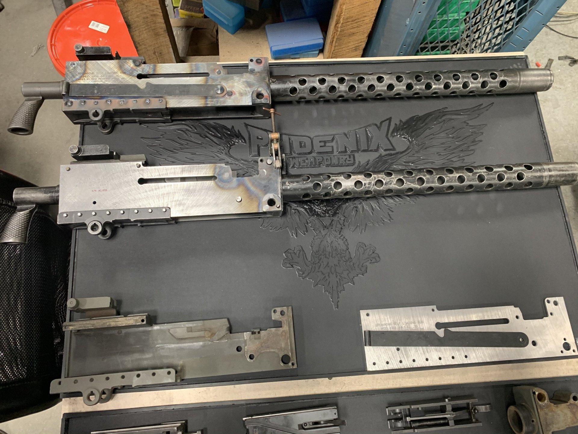 Disassembled machine gun parts on a work surface, including barrels and receiver components.