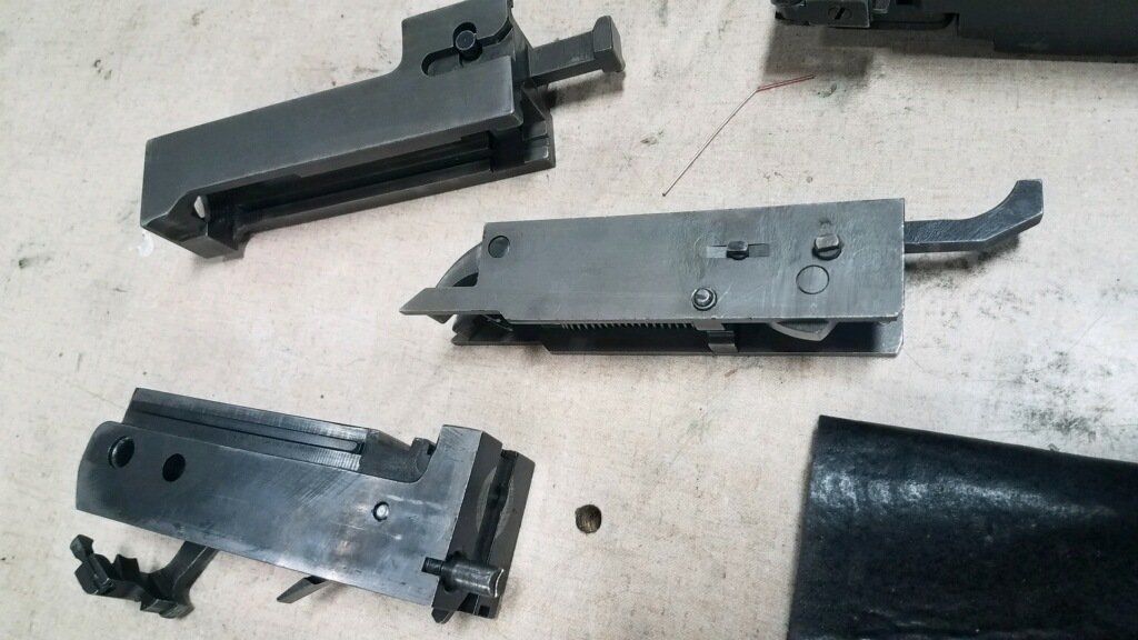 Disassembled gun parts, likely for cleaning or repair, laid out on a light-colored surface.
