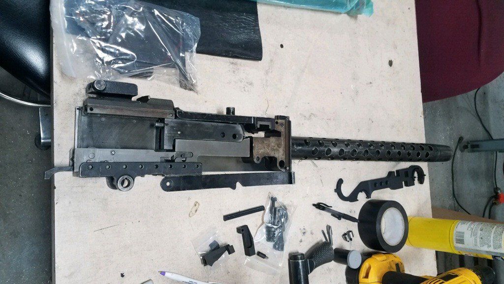 Disassembled heavy machine gun on a table with tools and parts, likely for maintenance or repair.
