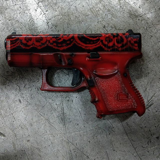 Red and black floral design Glock handgun on a concrete surface.