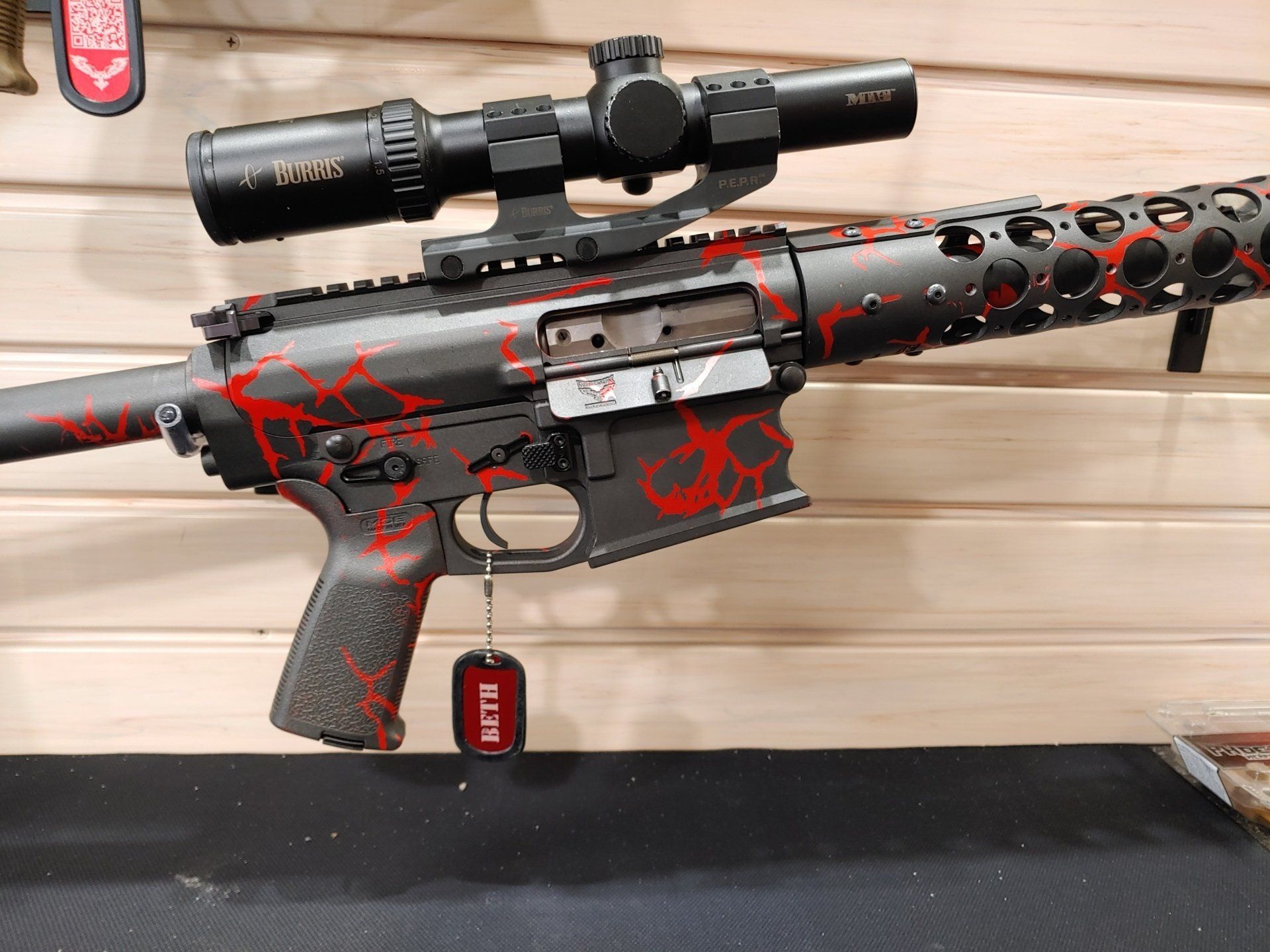 Black rifle with red accents, scope, and name tag