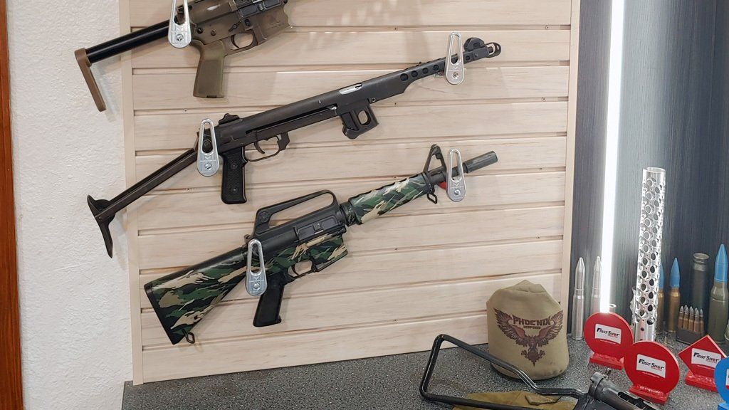 Guns secured with locks on a wooden display. Additional items like shells and a cap are nearby.