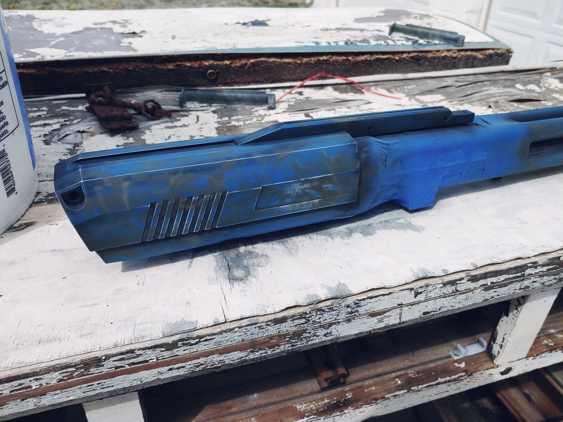 Blue painted rifle component on a weathered white surface, with other tools in the background.