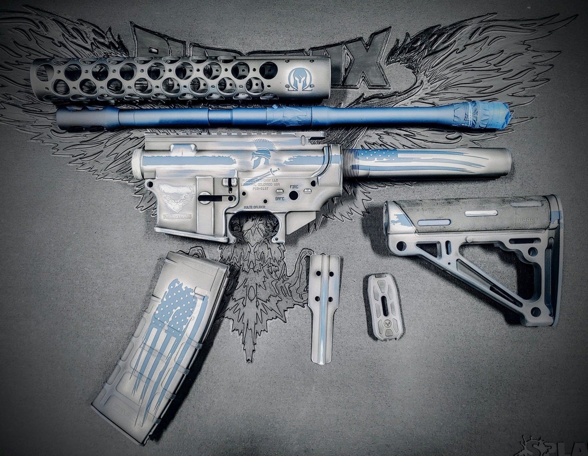 Disassembled AR-15 style rifle with blue accents and American flag magazine, laid out on a dark surface.