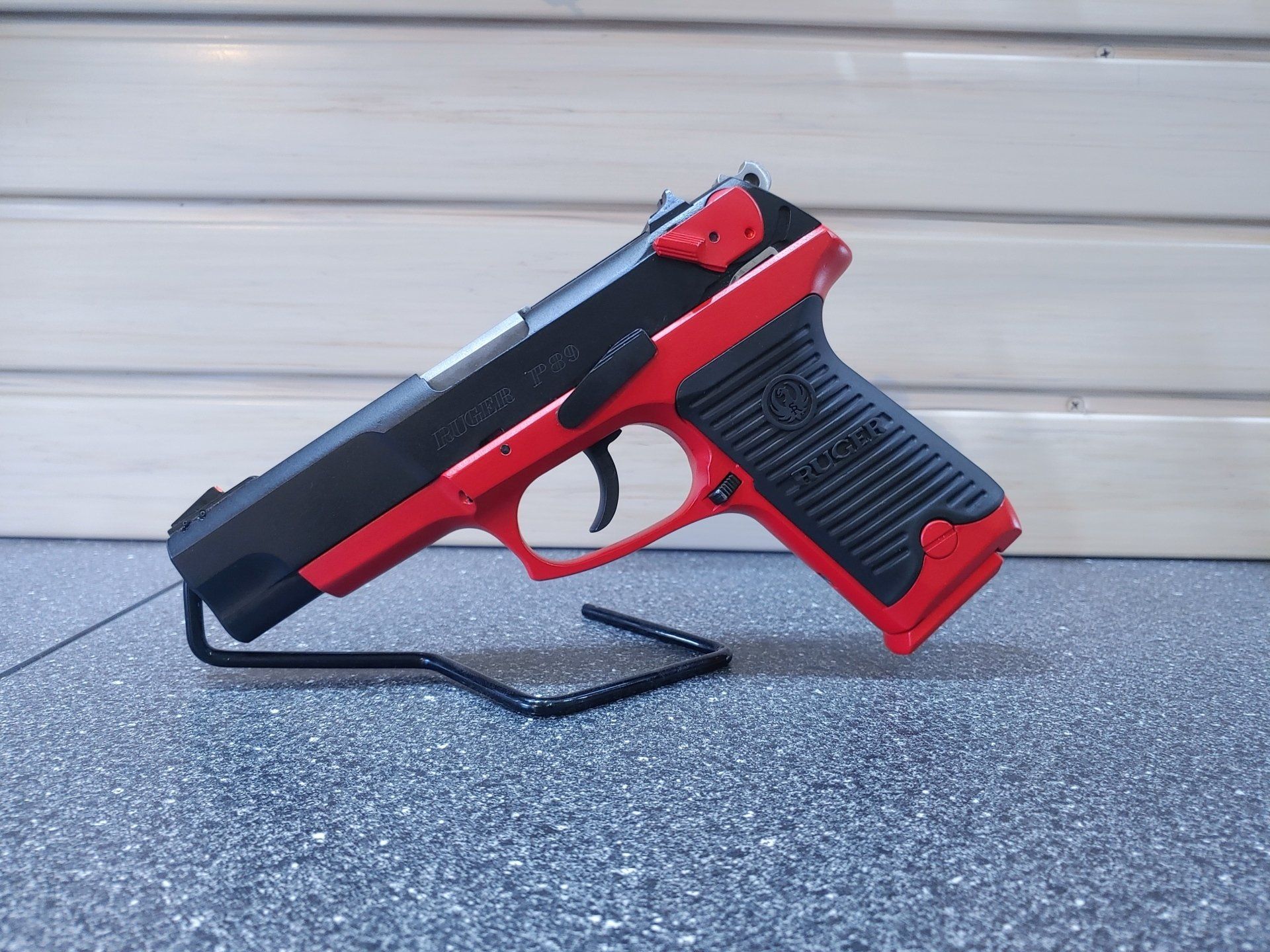 Black and red handgun on a display stand against a gray background.