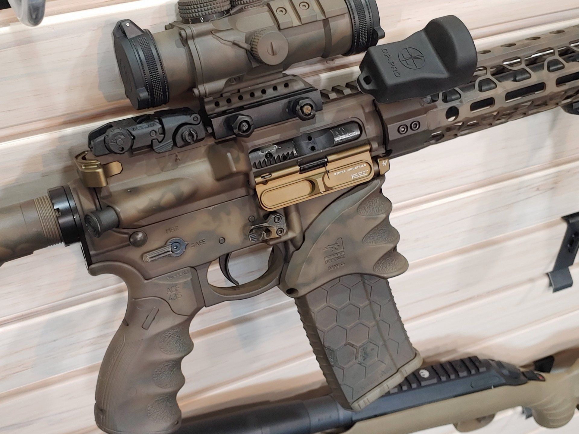 Tan and brown AR-15 style rifle with optic, angled foregrip, and loaded magazine on display.