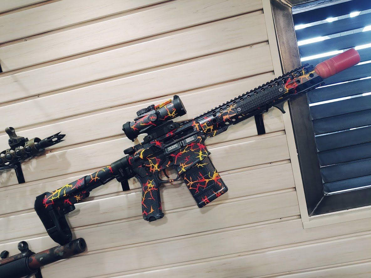 Black rifle with red, yellow, and orange camouflage pattern, mounted on a wall.