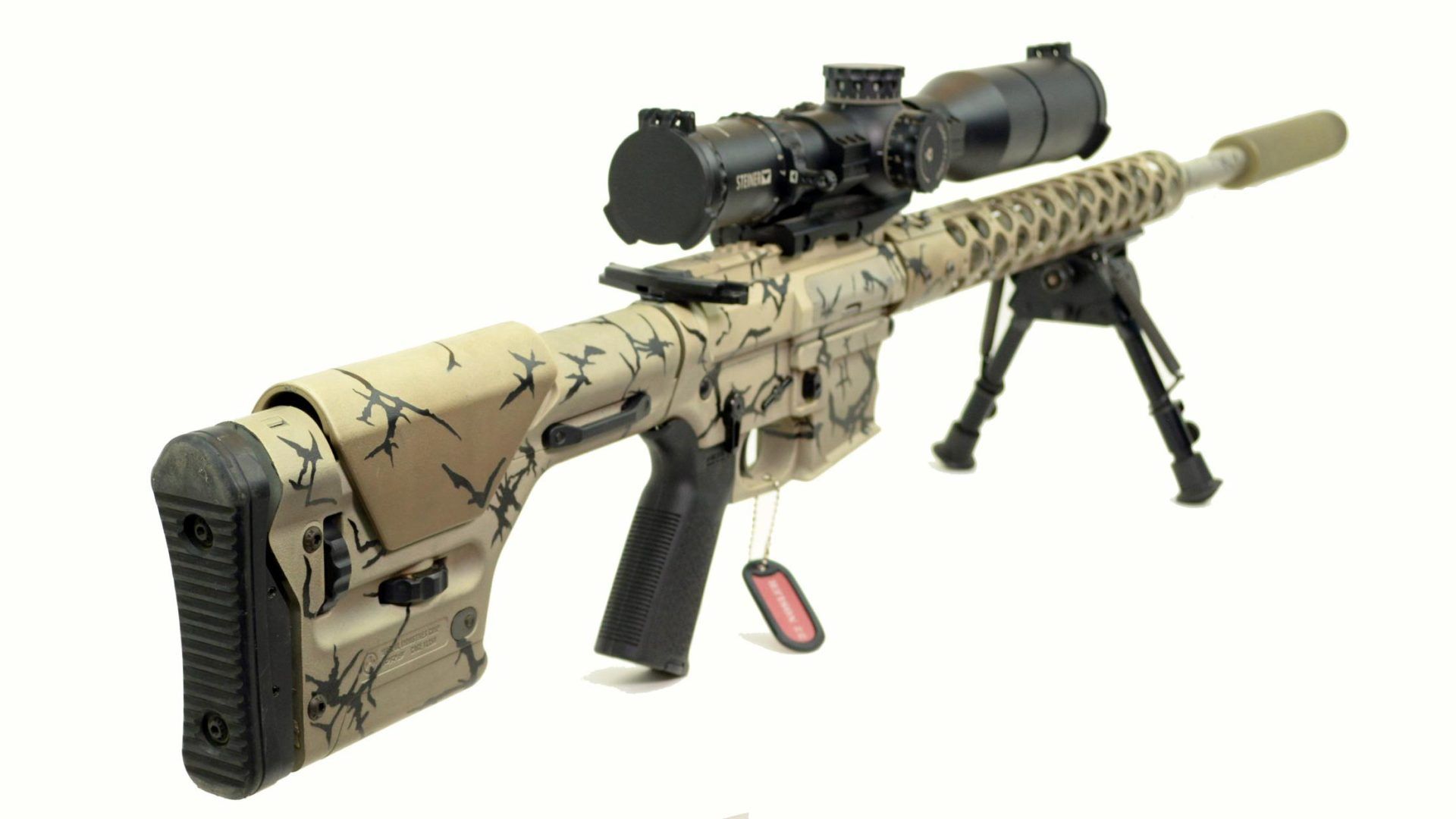 Camouflaged sniper rifle with scope, bipod, and silencer, on a white background.