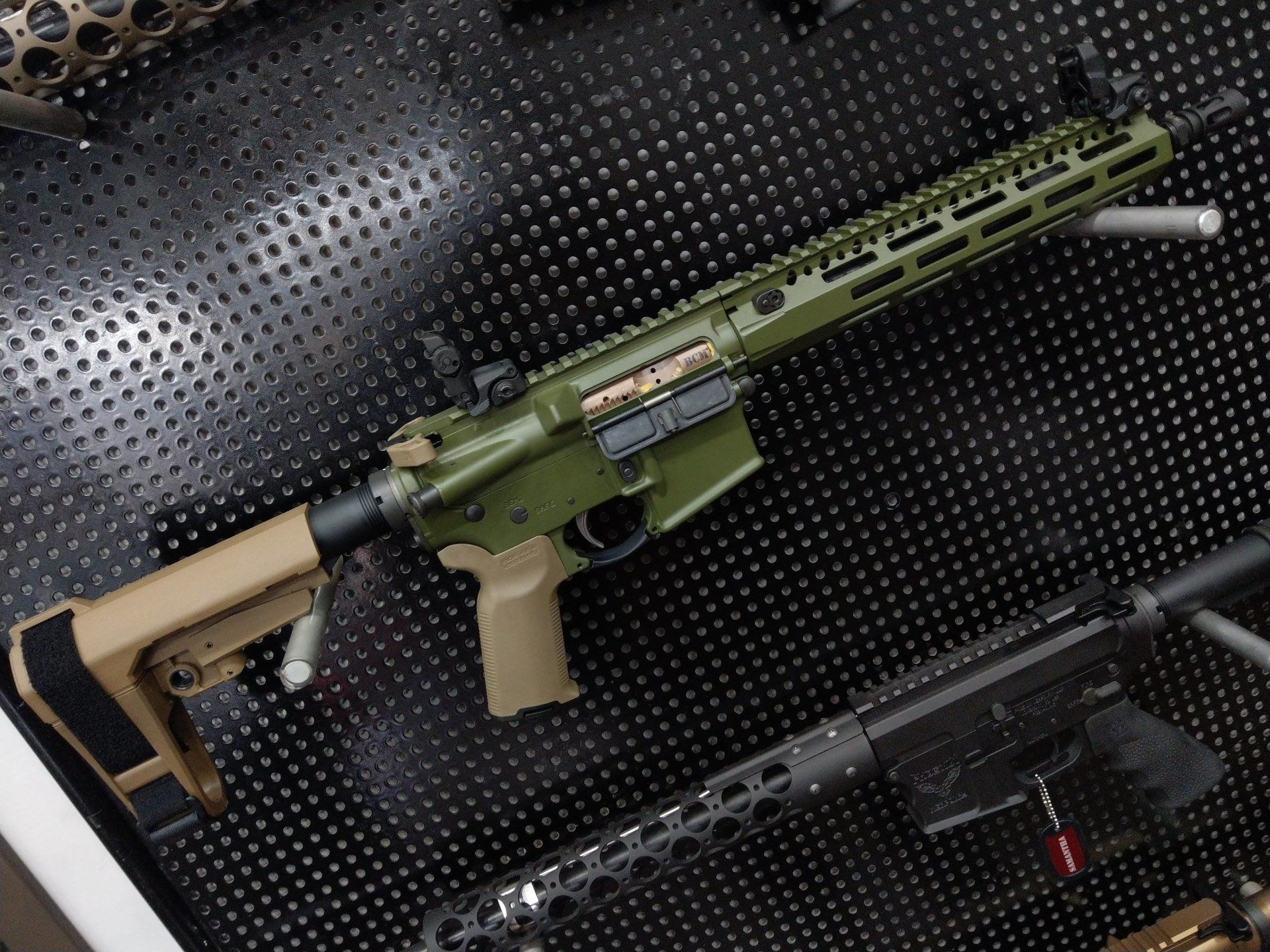 Green and tan AR-15 rifle on display; black surface with other firearms visible below.
