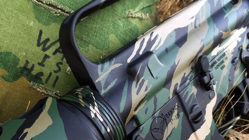 Close-up of a camo-painted AR-15 rifle. The words