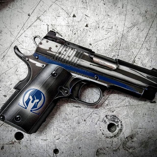 Black and silver handgun with blue accent and Spartan helmet logo on a metal surface.