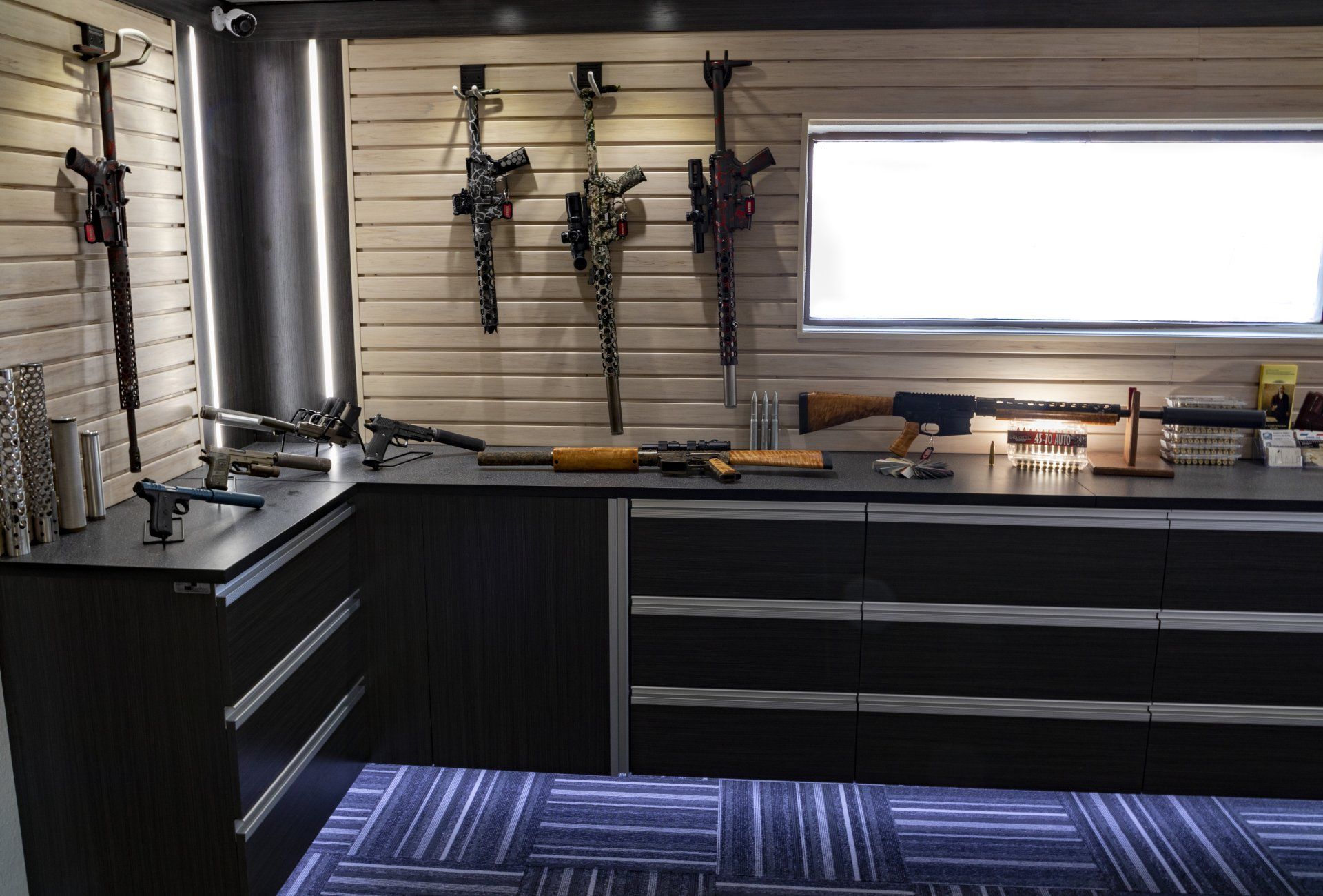 Firearms displayed on a counter and wall with drawers, against a light-toned wooden backdrop.
