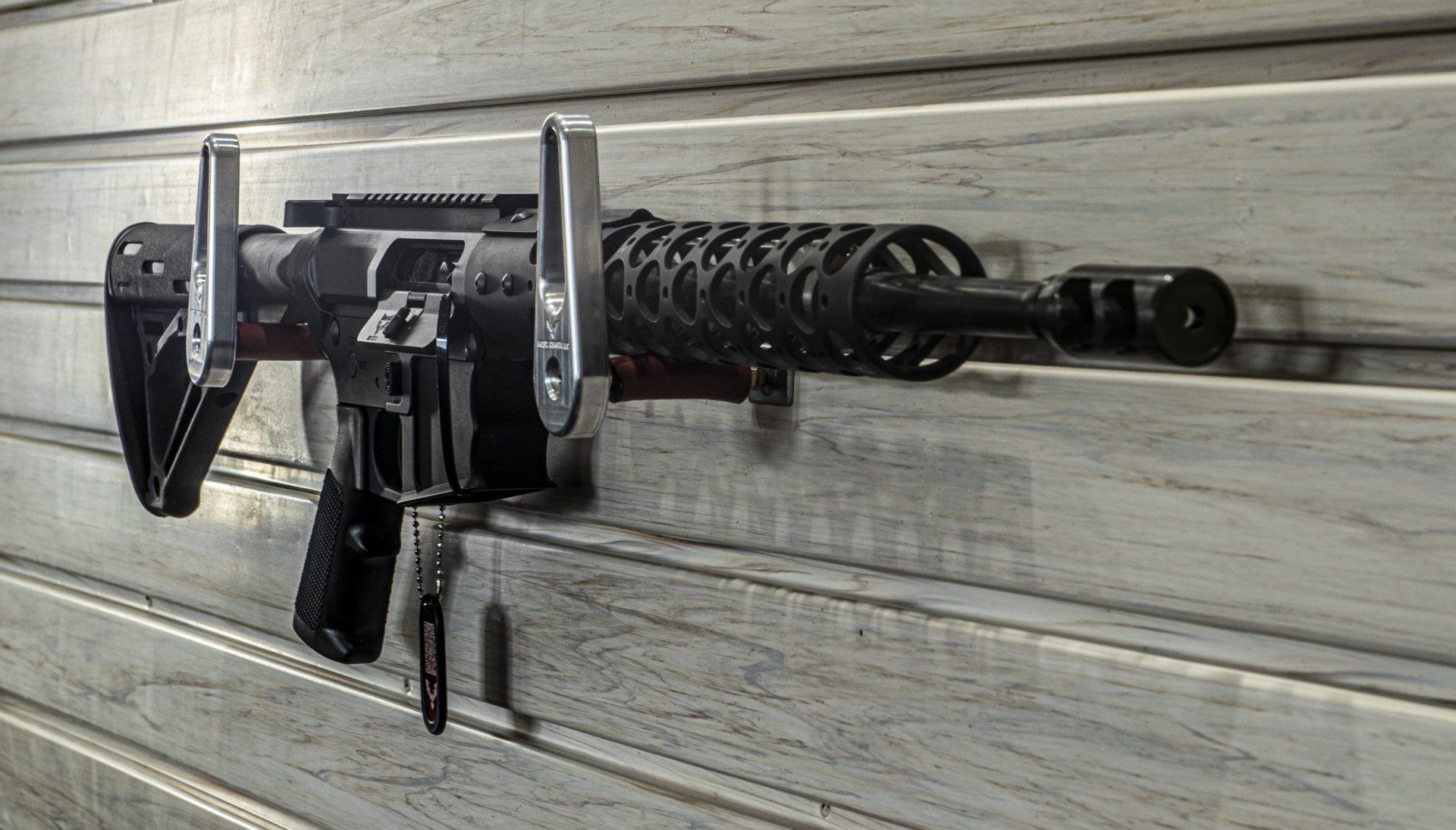 Black rifle mounted on a light-colored wooden wall.