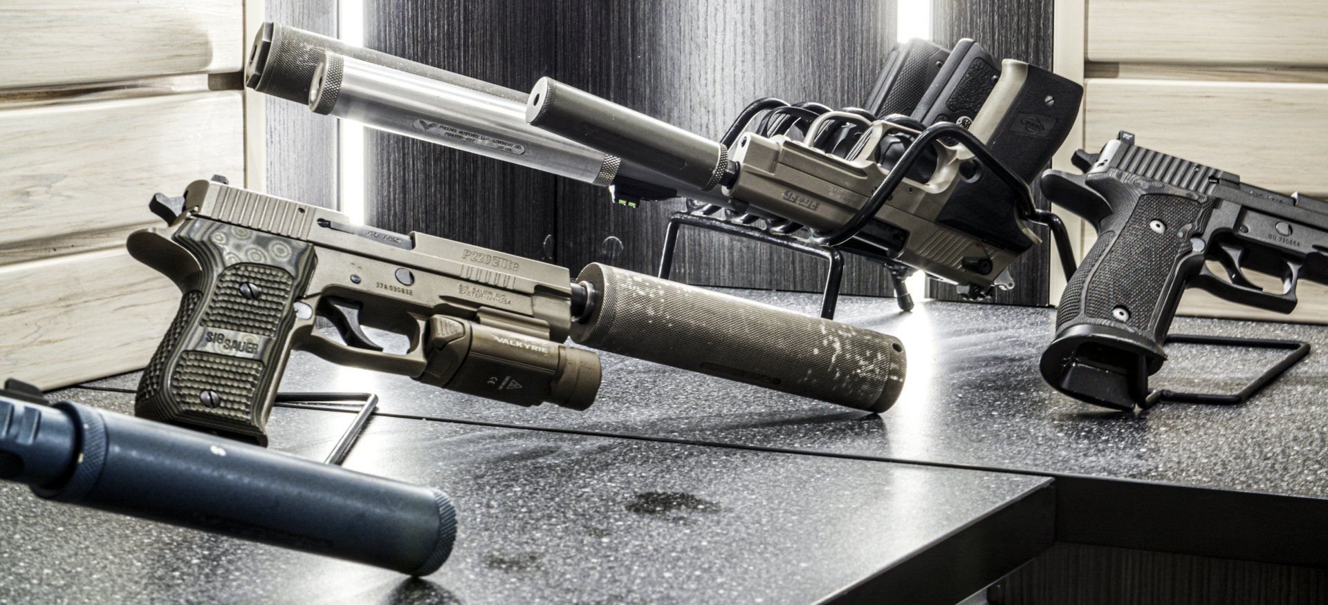 Guns with silencers on a wet tabletop. One has a light attached.