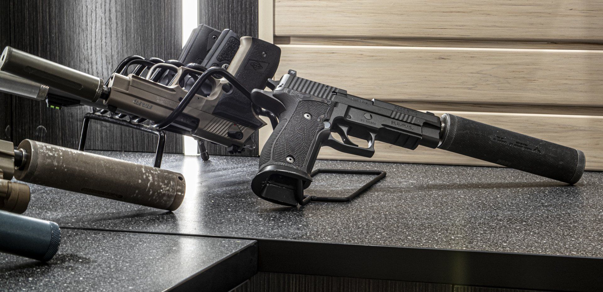 A black handgun with a silencer, resting on a table with other gun accessories.